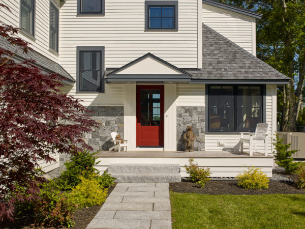 Exterior view of entry. Granite path and steps lead to extended landing. Welcoming red door flanked by stone and wood siding.