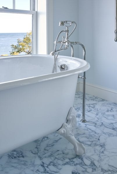 A close-up of the white clawfoot tub with vintage faucet, marble flooring, and views of the coast.