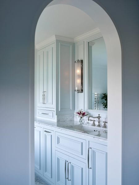 An arched doorway to the bright bathroom with marble countertops.