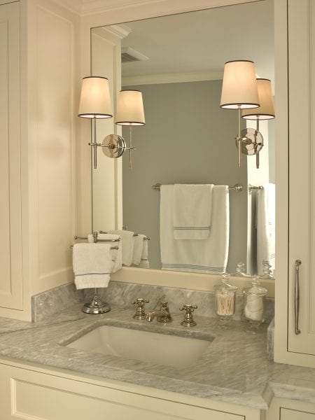 An ivory vanity with gray marbled countertop and large mirror.