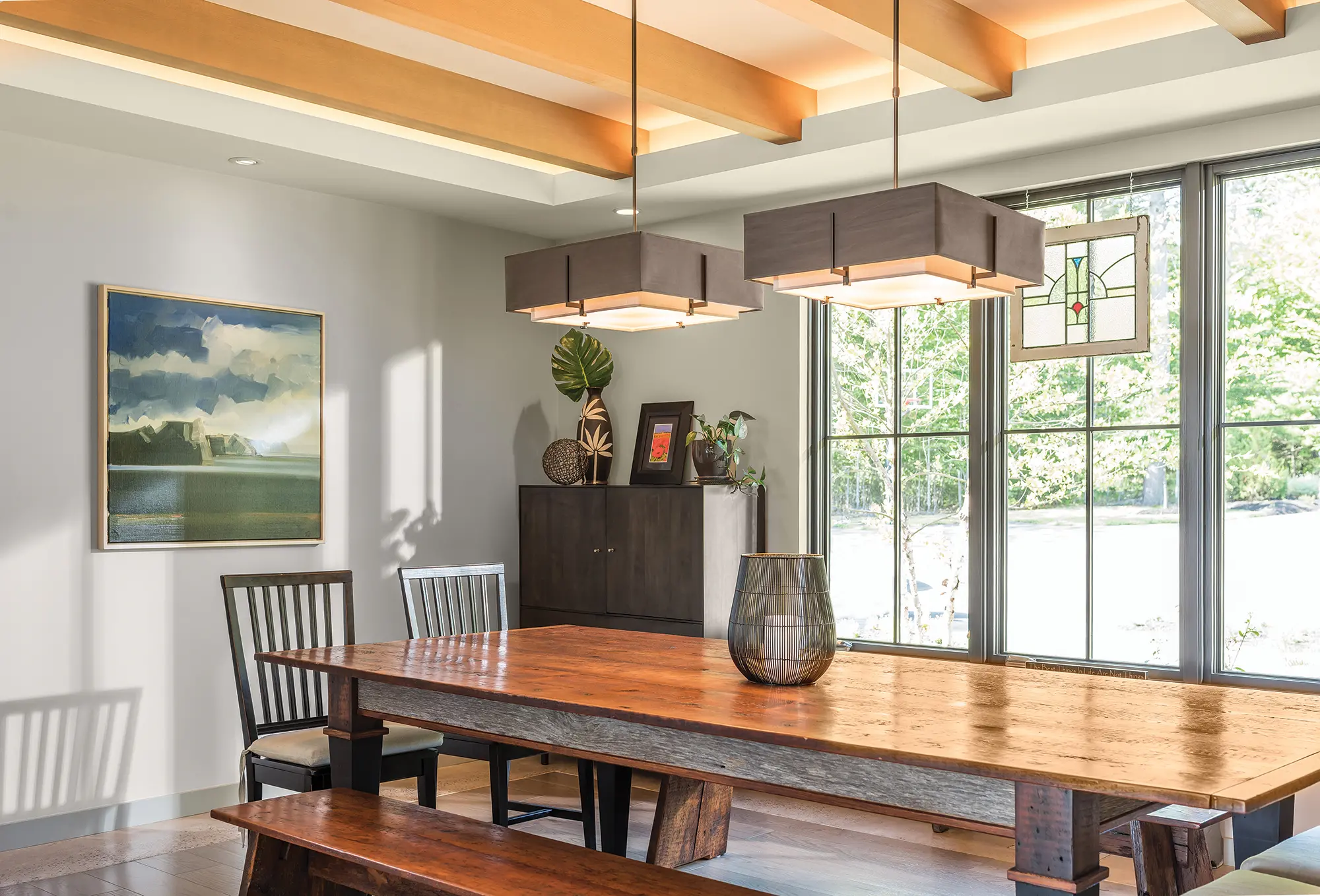 A contemporary dining area with large table, bench seats, stained glass artwork, and large windows.